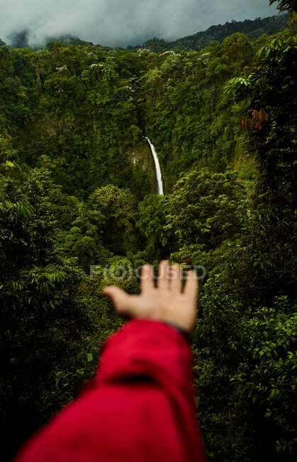 Unerkennbare Person demonstriert wunderbaren Wasserfall im grünen Regenwald an bewölkten Tag in Costa Rica — Stockfoto