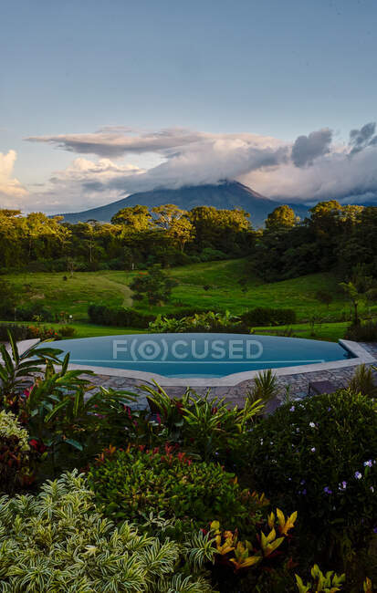 Piscina con agua limpia ubicada cerca de plantas exóticas en valle verde cerca del pico de la montaña en la noche nublada en Costa Rica - foto de stock