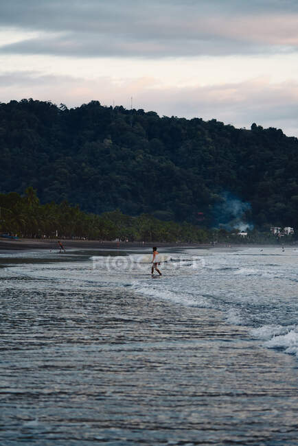 Unbekannter Mann mit Surfbrett läuft an bewölktem Abend am Strand von Costa Rica in Meeresnähe — Stockfoto