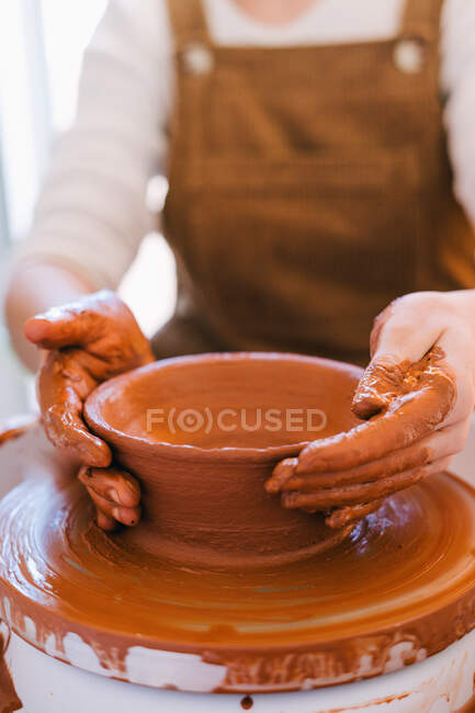 Alto ángulo de persona de la cosecha en ropa casual haciendo cerámica hecha a mano utilizando equipo especial mientras se trabaja en estudio contemporáneo ligero - foto de stock