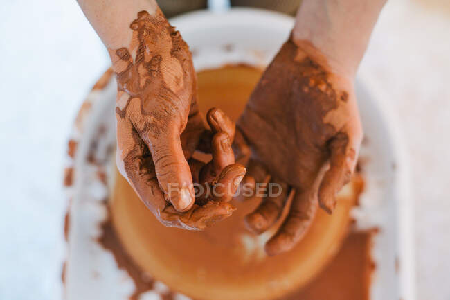 De cima de mãos de pessoa de colheita em barro marrom depois de fazer cerâmica contra equipamento especial borrado na oficina moderna leve — Fotografia de Stock