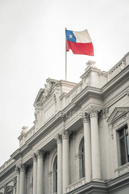 From below amazing exterior of Palacio de los Tribunales de Justicia with white walls and columns in composition with beautiful small decor elements in neoclassic style and national flag of republic Chile on top — Stock Photo