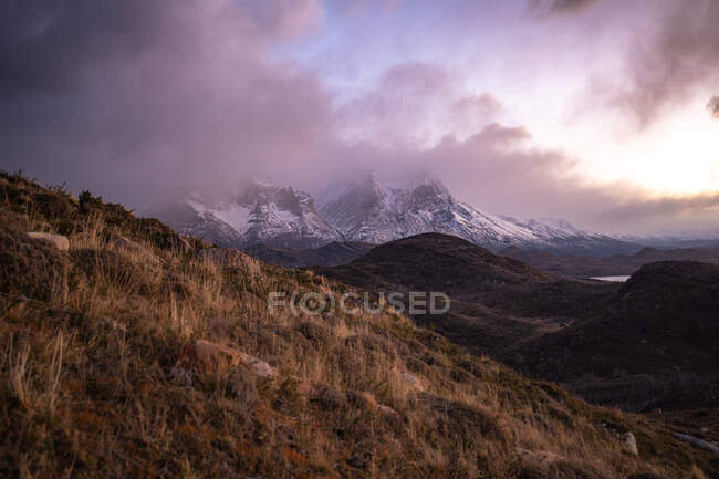 Pintoresco paisaje de tierras altas silvestres con picos de montañas nevadas y crestas entre nubes dramáticas durante el atardecer - foto de stock