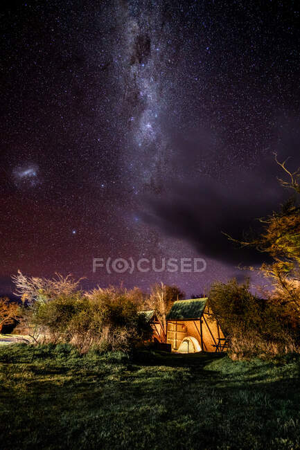 Magnificent scenery with solitary camp on glade among trees under violet clear sky with Milky Way among much of stars — Stock Photo