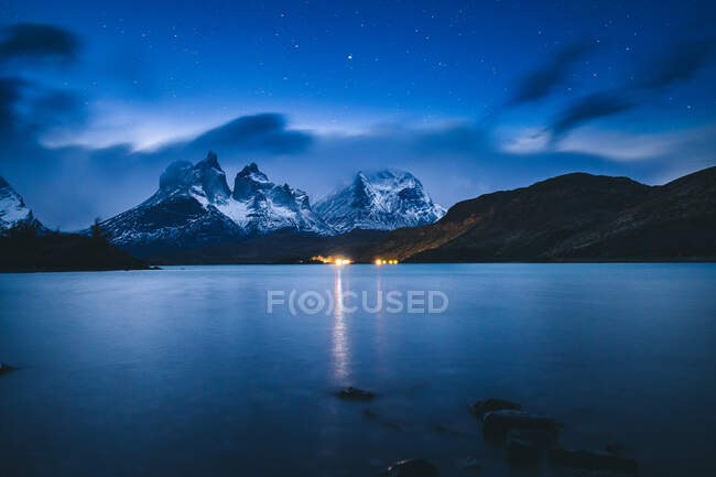 Cenário de tirar o fôlego de lago tranquilo sob céu estrelado claro contra rochas nevadas na noite tranquila — Fotografia de Stock