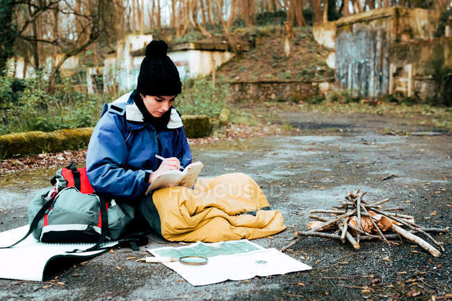 Jovem mochileiro feminino fazendo anotações na fogueira — Fotografia de Stock