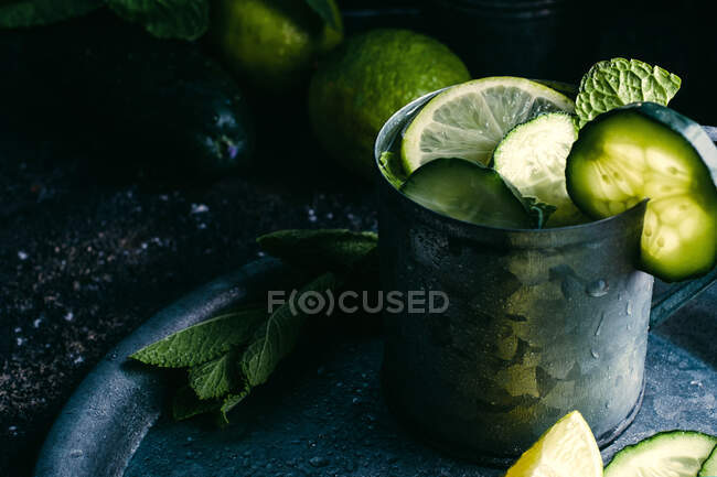 De arriba taza de metal de bebida fría de desintoxicación de pepino con rodajas de lima y hojas de menta colocadas en bandeja - foto de stock