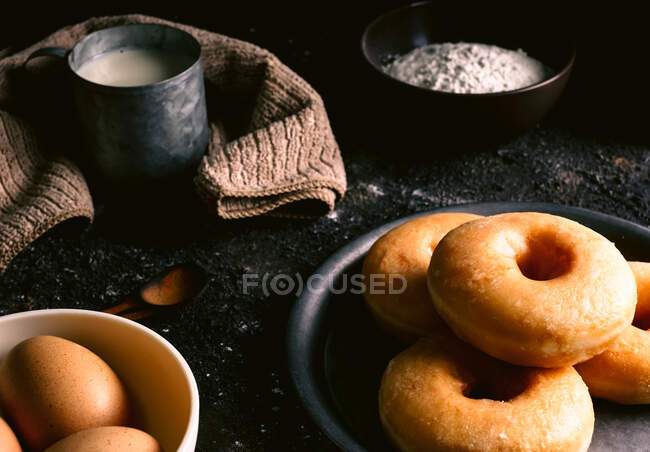 From above of fresh doughnuts placed on rough table near various pastry ingredients and utensils in kitchen — Stock Photo