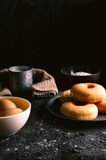 Beignets frais placés sur une table rugueuse près de divers ingrédients et ustensiles de pâtisserie dans la cuisine — Photo de stock
