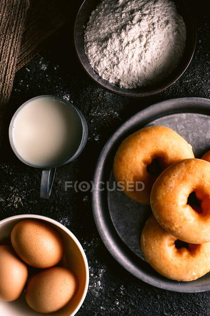Vista superior de donuts frescos colocados em mesa áspera perto de vários ingredientes de pastelaria e utensílios na cozinha — Fotografia de Stock