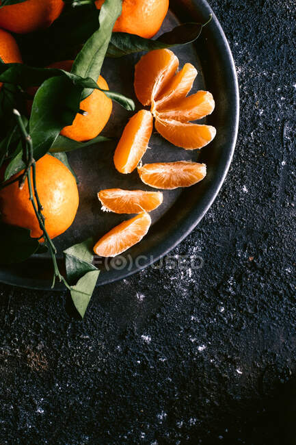Top view of mug with fresh fruit juice and plate with ripe tangerines placed on rough black table near napkin — Stock Photo