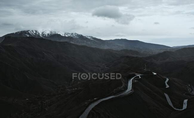 Зверху порожня асфальтована звивиста дорога на чорних потужних горах з хмарно-сірим небом на фоні — стокове фото