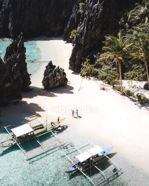 Vue aérienne de la côte avec sable blanc et les touristes près de voiliers sur l'île avec de gros rochers à elnido, philippines — Photo de stock