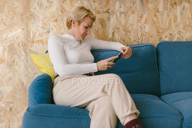 Mulher de negócios adulta com penteado curto sentado no lazer no sofá e navegando telefone celular no escritório — Fotografia de Stock