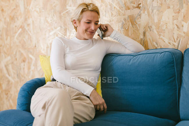 Donna d'affari adulta con acconciatura corta seduta nel tempo libero sul divano e navigando sul cellulare in ufficio — Foto stock