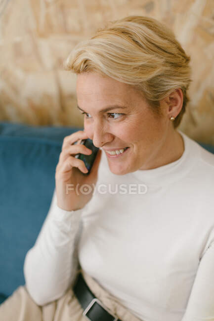 Зверху блондинка з коротким волоссям розмовляє на мобільному телефоні обговорюючи бізнес, посміхаючись — стокове фото