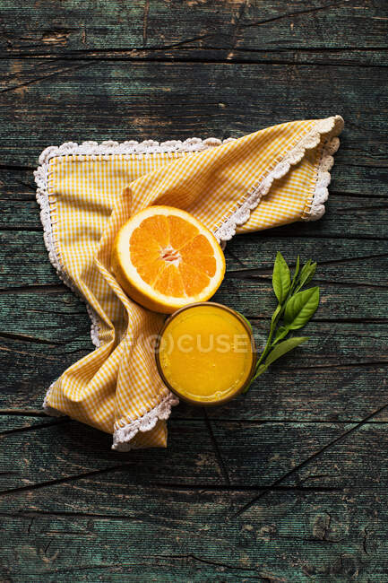 Ein Glas frisch gepresster Orangensaft in der Nähe von Hälften frisch geschnittener Orangen auf einem dunklen rustikalen Holztisch vor dunklem Hintergrund — Stockfoto