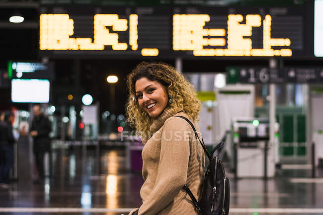 Side view of beautiful happy woman looking at camera with backpack in airport terminal — Stock Photo