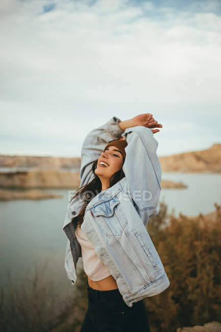Vista lateral de la alegre joven encantadora turista mirando hacia otro lado mientras disfruta de viaje de fin de semana al lago en otoño - foto de stock