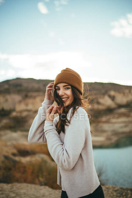 Vista lateral de la feliz joven encantadora turista mirando a la cámara mientras disfruta de viaje de fin de semana al lago en otoño - foto de stock