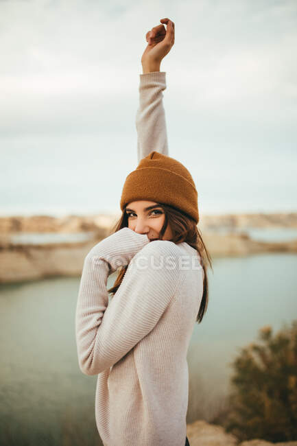 Вид сбоку на счастливую молодую очаровательную туристку, смотрящую в камеру во время путешествия на выходные на озеро осенью — стоковое фото