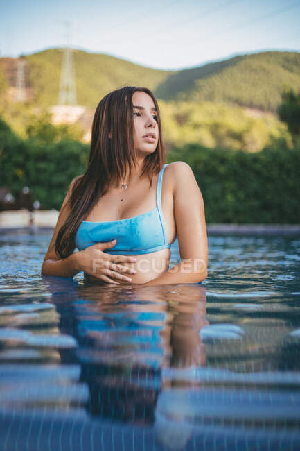 Нижче чуттєвої молодої чарівної самиці в купальнику, яка дивиться у далечінь, стоячи на дні озера в сільській місцевості. — стокове фото