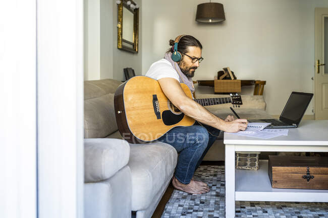 Contemporary man with guitar writing chords in living room — Stock Photo