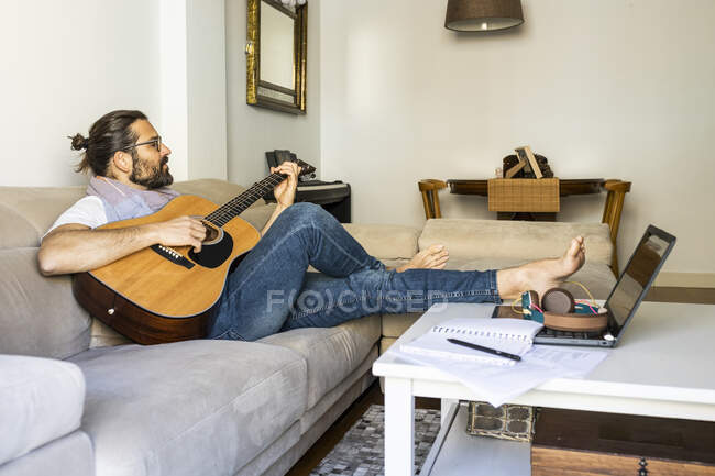 Stylish guitarist on couch in living room — Stock Photo