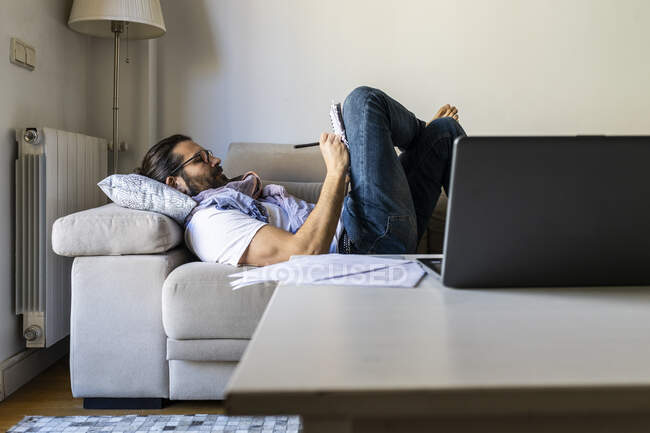 Mann schreibt Notizen auf Couch im gemütlichen Wohnzimmer — Stockfoto