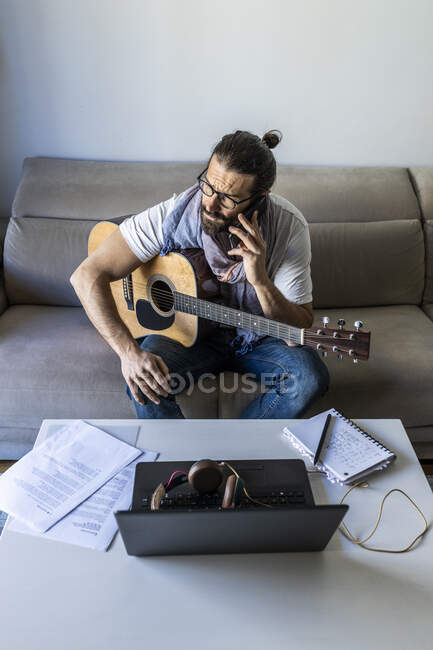 Junger männlicher Musiker ruft Smartphone im Wohnzimmer an — Stockfoto