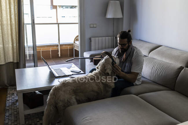 Casual guy putting headphones on dog in living room — Stock Photo