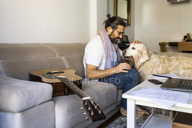 Tipo casual poniendo auriculares en el perro en la sala de estar - foto de stock