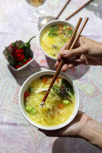 From above cropped unrecognizable person holding a bowl of oriental ramen healthy noodles soup with shiitake, spinach, carrots, eggs and chillies on restaurant table — Stock Photo