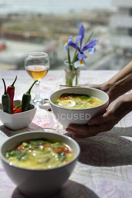 De cima cortado pessoa irreconhecível segurando uma tigela de ramen oriental sopa de macarrão saudável com shiitake, espinafre, cenouras, ovos e pimentas na mesa do restaurante — Fotografia de Stock