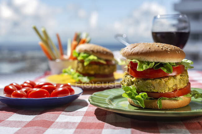 Hamburguesa de lenteja verde vegana sana casera con tomate, lechuga y papas fritas con copa de vino tinto - foto de stock