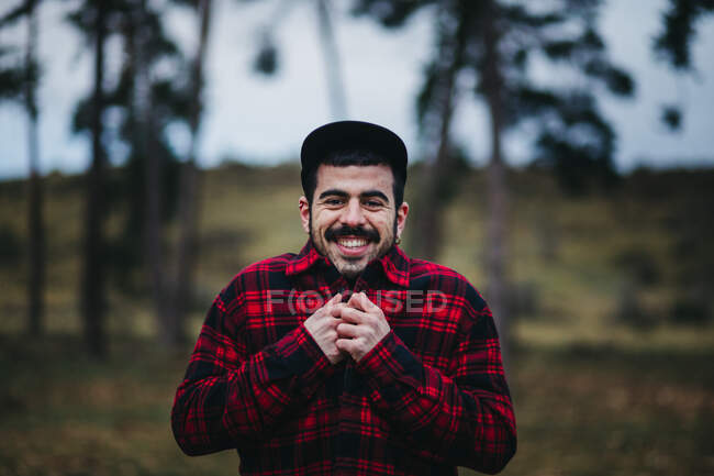 Cheerful man in casual wear standing among evergreen coniferous trees in autumn countryside — Stock Photo