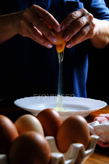Femme méconnaissable brisant oeuf de poulet frais dans un bol pendant la cuisson de la pâtisserie dans la cuisine — Photo de stock