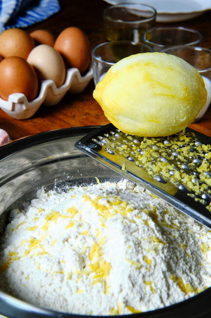 Vista dall'alto della grattugia fresca di limone e metallo posta sulla ciotola con farina e buccia durante la preparazione della pasta frolla in cucina — Foto stock