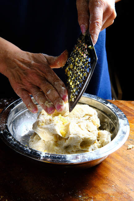Unrecognizable female removing fresh lemon peel from metal grater over bowl with pastry dough in kitchen — Stock Photo