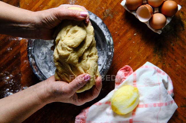 С вышесказанного анонимная женщина месит свежее тесто за столом с лимоном и салфеткой во время приготовления выпечки дома — стоковое фото