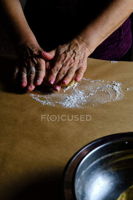 Невпізнавана дама прокатує маленькі кульки з м'якого тіста під час приготування тіста на столі на кухні — стокове фото