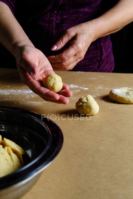 Irriconoscibile signora rotolamento palline da pasta morbida durante la cottura pasticceria sul tavolo in cucina — Foto stock