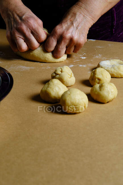 Невпізнавана дама прокатує маленькі кульки з м'якого тіста під час приготування тіста на столі на кухні — стокове фото