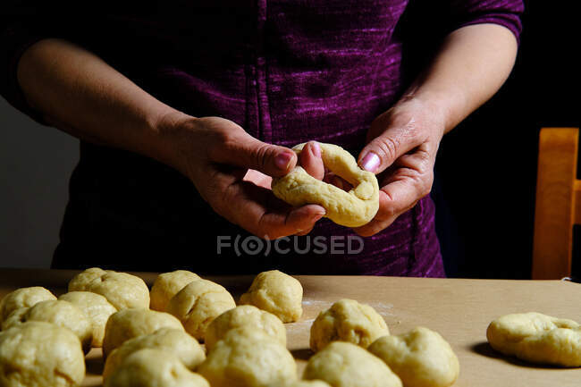 Анонимная женщина делает кольца из мягкого теста во время приготовления пончиков за столом на кухне — стоковое фото