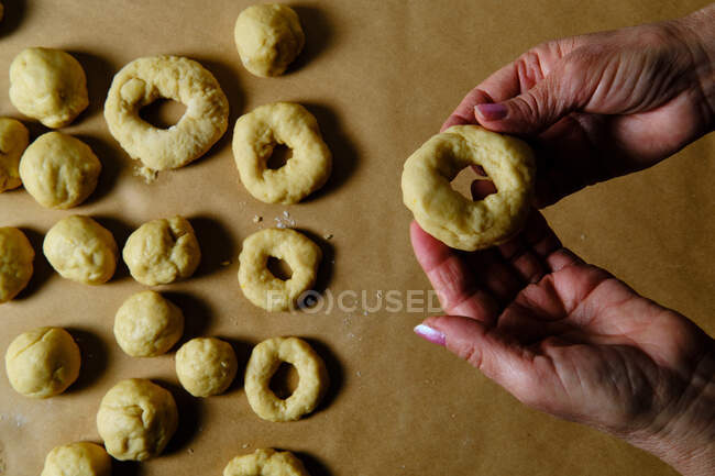 Vista superior da mulher anônima fazendo anéis de massa macia enquanto prepara donuts sobre mesa na cozinha — Fotografia de Stock