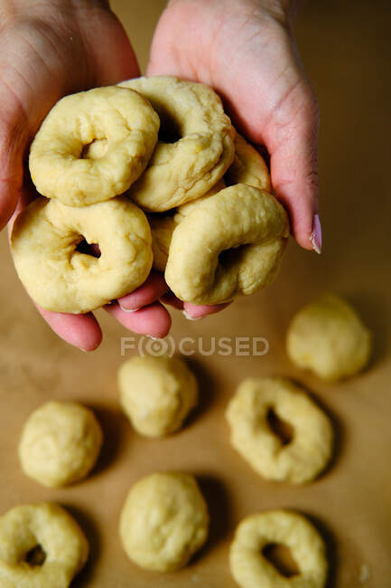 Сверху анонимная женщина делает кольца из мягкого теста во время приготовления пончиков за столом на кухне — стоковое фото
