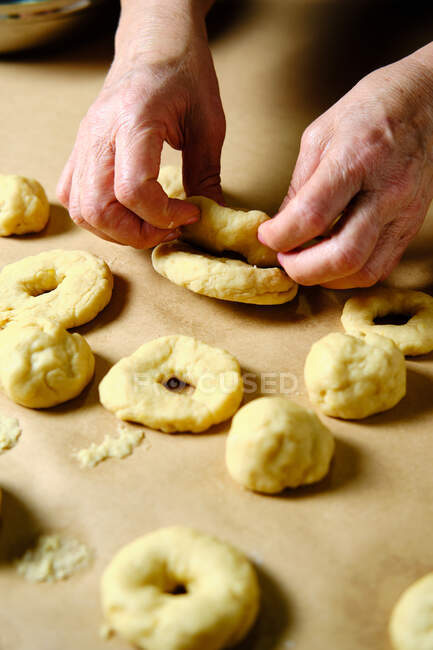 Зверху анонімна жінка робить кільця з м'якого тіста під час приготування пончиків над столом на кухні — стокове фото