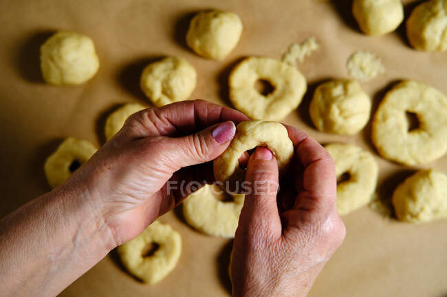 Vista superior da mulher anônima fazendo anéis de massa macia enquanto prepara donuts sobre mesa na cozinha — Fotografia de Stock