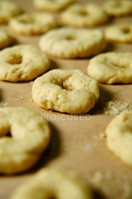 De acima mencionados anéis da massa de farinha suave enquanto prepara rosquinhas sobre a mesa na cozinha — Fotografia de Stock