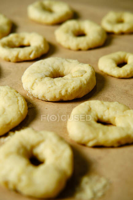 De acima mencionados anéis da massa de farinha suave enquanto prepara rosquinhas sobre a mesa na cozinha — Fotografia de Stock